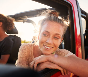 Millennial white couple on a road trip driving in open top car, women leaning on car door, close up